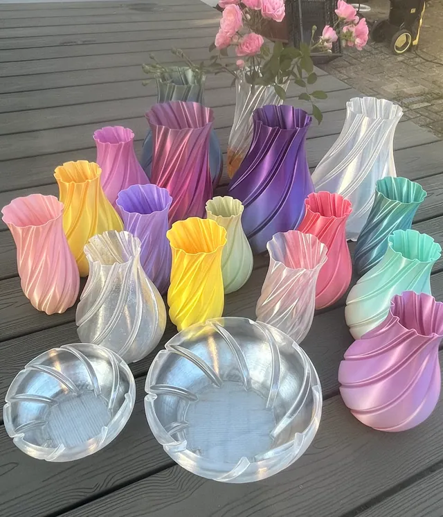 Bunte Spiralvasen aus dem 3D-Drucker mit Farbverlauf, aufgestellt auf einem Ständer aus Filamentspulen